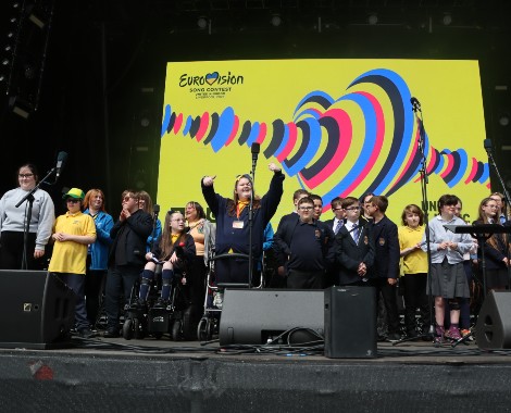 School children on stage in from of a yellow Eurovision 2023 screen.